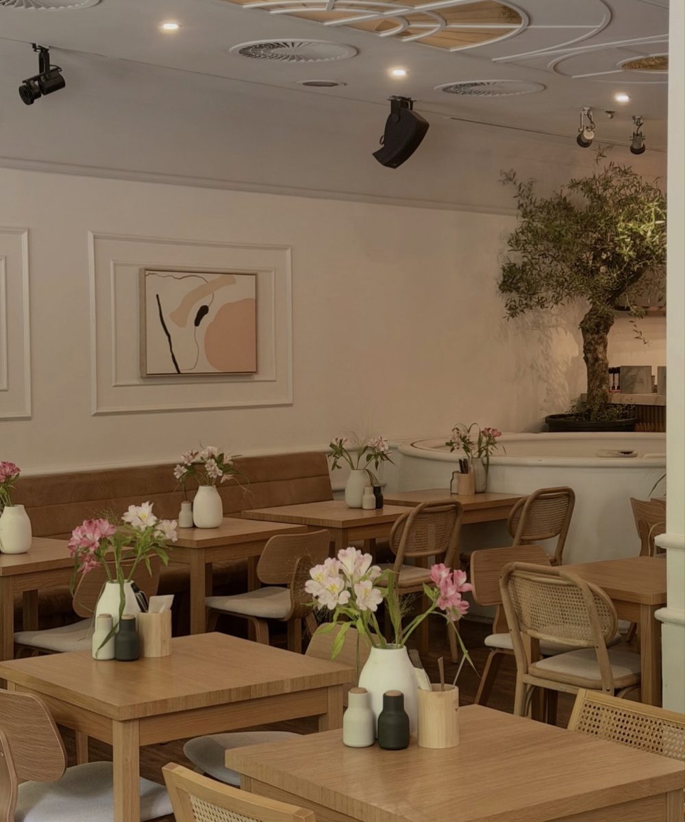 Innenraum des marmell café Freiburg mit Holztischen, Blumen und Olivenbaum